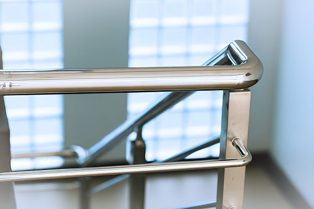 Close-up of a modern stainless steel railing with a glass wall in the background.